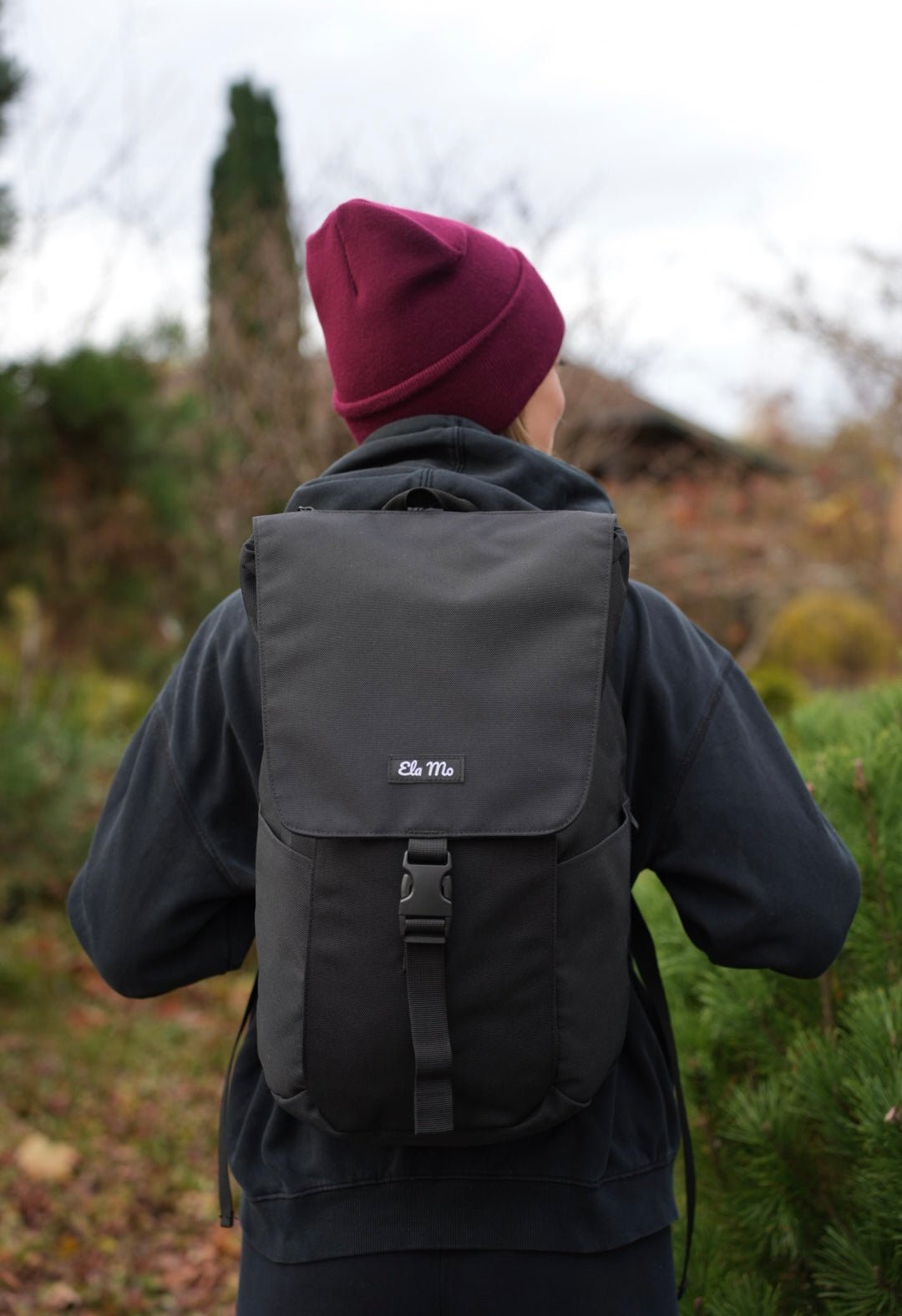 Ela Mo™ Everywhere Daypack | Black. Eine Frau mit einem schwarzen Rucksack im Wald – täglicher Lifestyle.