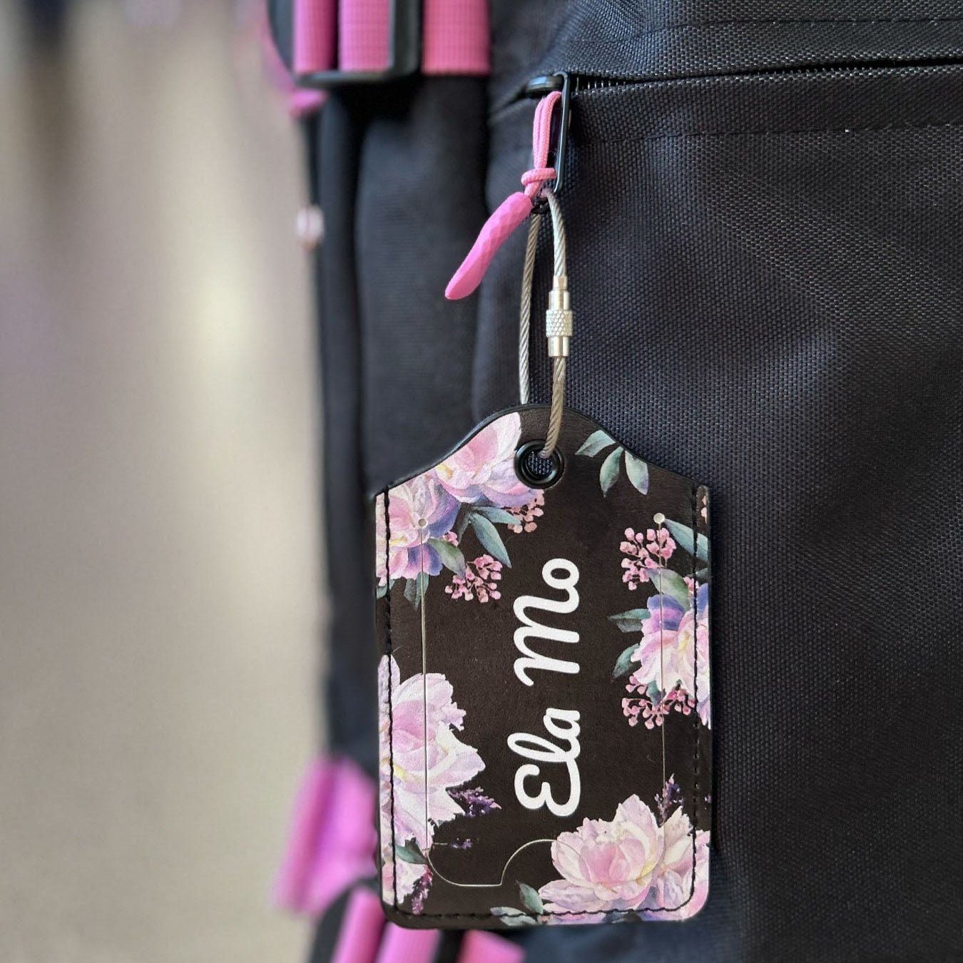 Ela Mo™ Gepäckanhänger | Beauty in Darkness. Ein geblümter Anhänger an einem Reißverschluss des Rollkoffers.