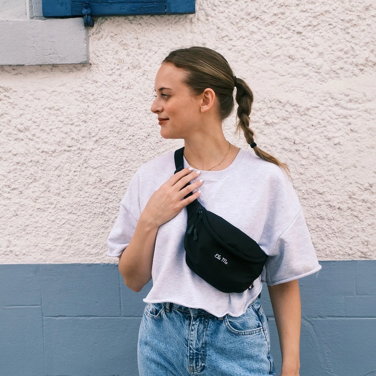 Ela Mo™ Hipbag | Black. Eine Frau mit Hipbag an einem sonnigen Tag auf der Straße.