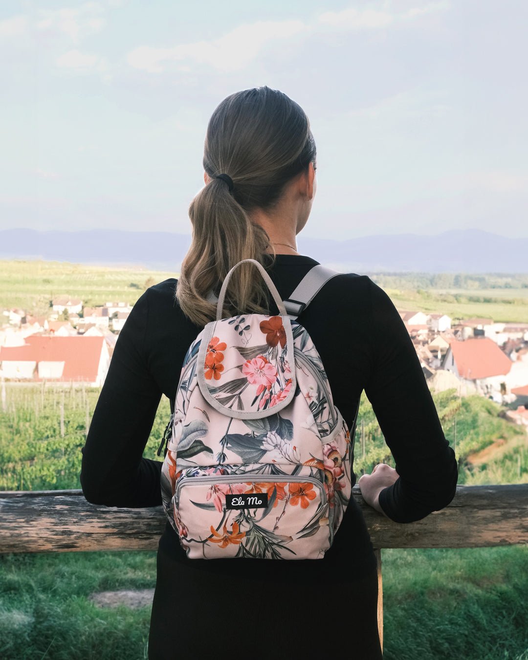 Ela Mo™ Mini Rucksack | Luxe. Eine Frau mit dem Rucksack an einem sonnigen Tag, Ansicht von hinten.