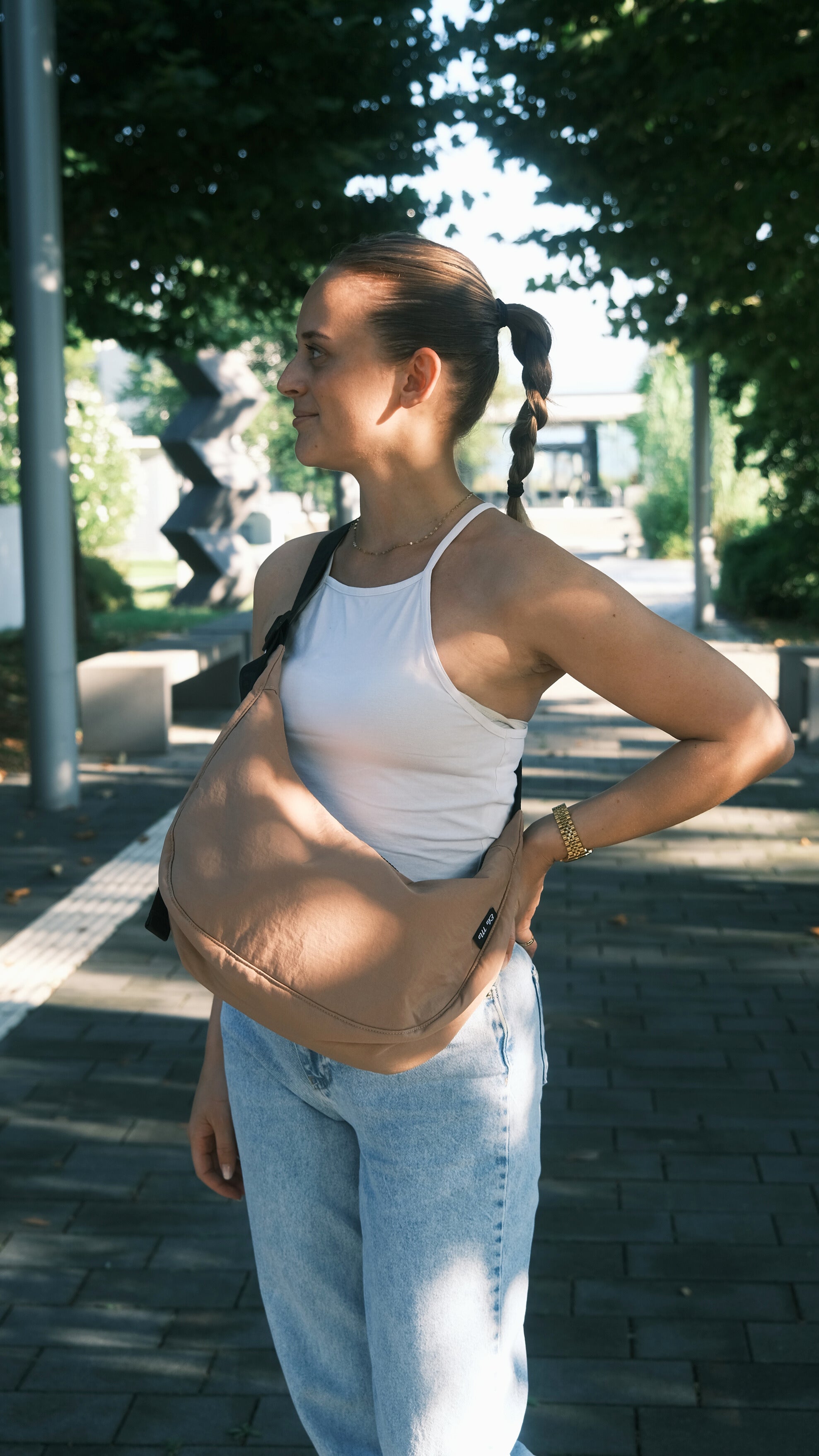 Ela Mo™ Moon Bag | Cocoa. Eine Frau mit der Tasche im Sommer auf der Straße – alltäglicher Lifestyle.
