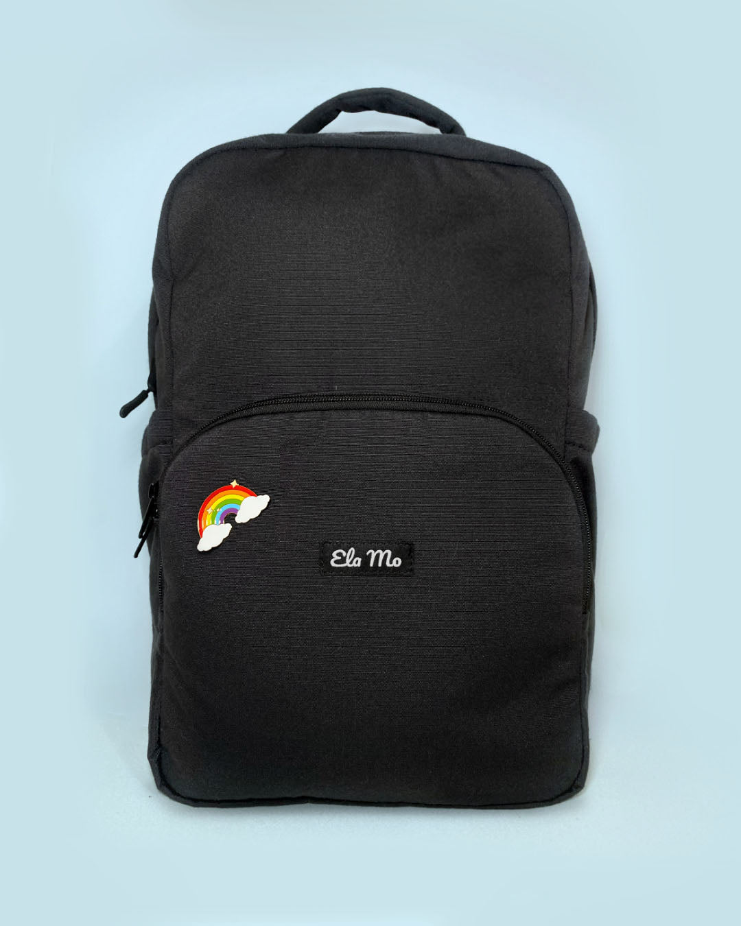 Ela Mo™ Pin für Rucksäcke| Rainbow. Ein kleiner Pin ist vorne am schwarzen Rucksack befestigt.