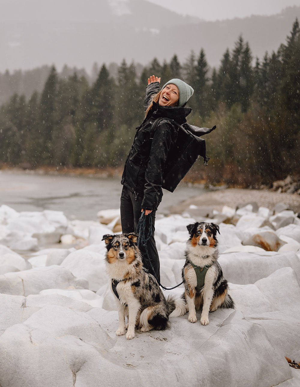 Ela Mo™ Regenjacke | Black. Frau in schwarzer Regenjacke mit zwei Hunden im regnerischen Wald.