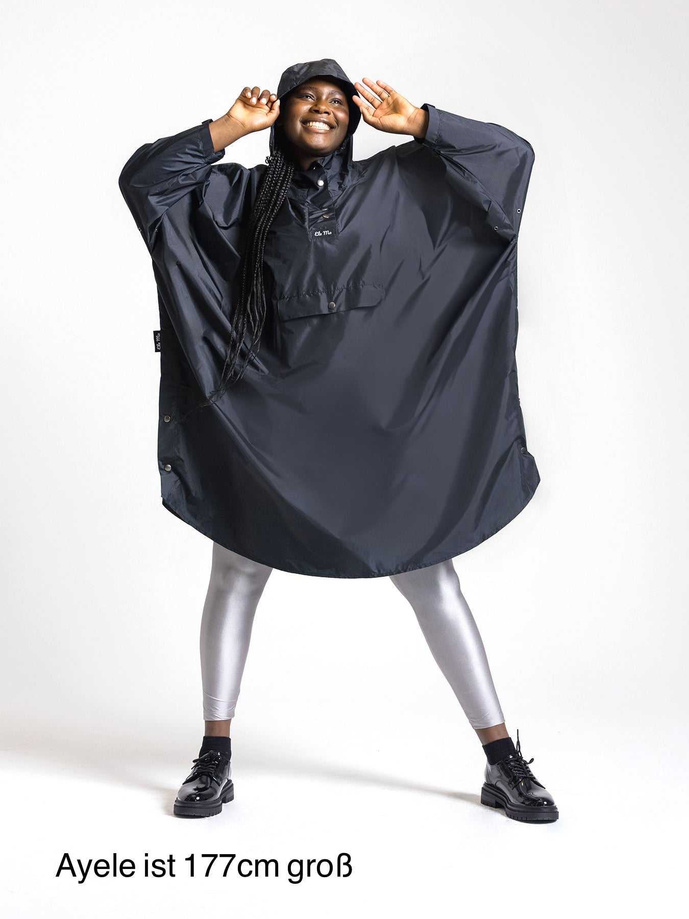Ela Mo™ Regenponcho | Black. Eine Frau mit Regenponcho, inklusive Produkt-Höhenangabe.