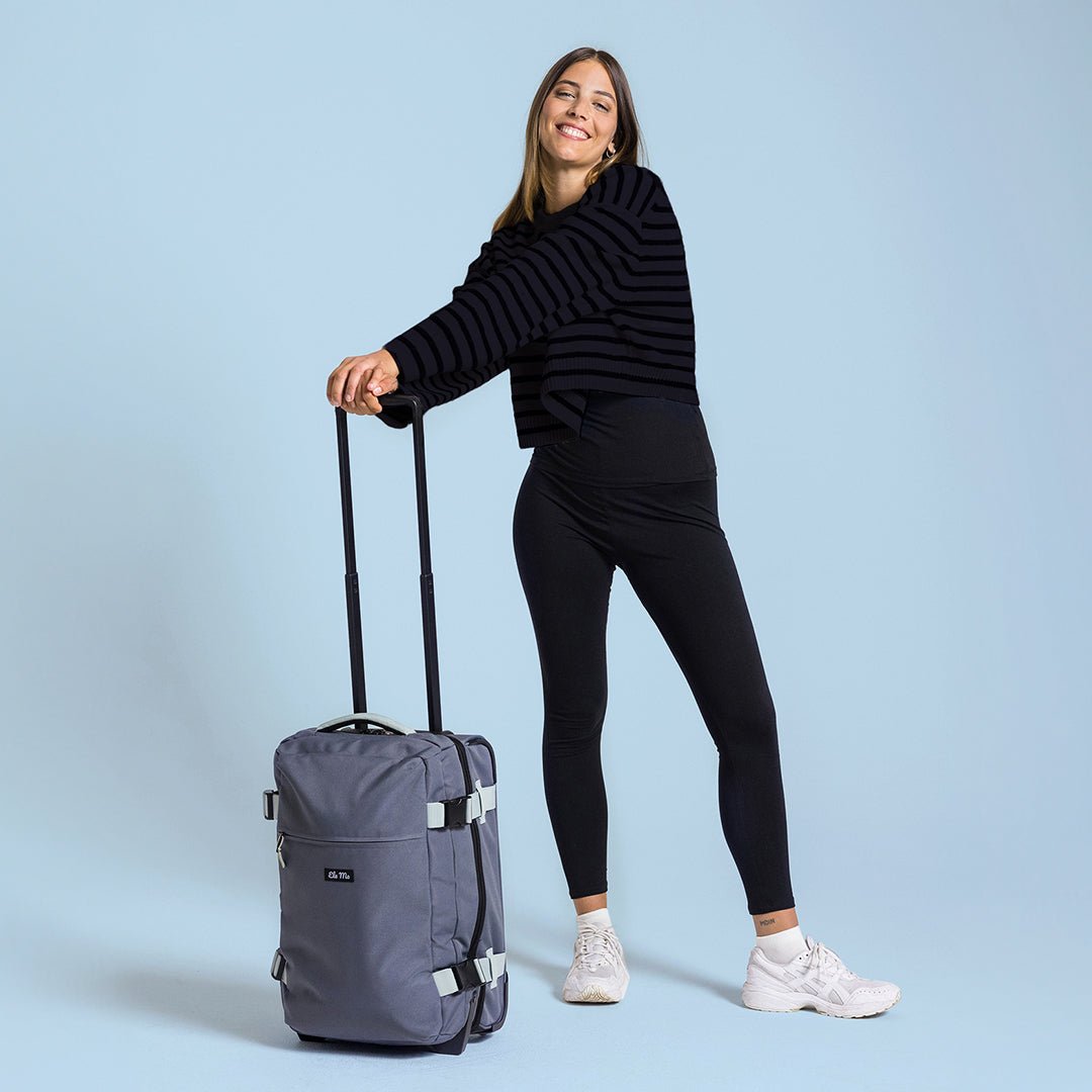 Ela Mo™ Reisetasche mit Rollen 42 Liter | Darkgrey Mint. Eine Frau neben einer Reisetasche mit hochgezogenem Griff.
