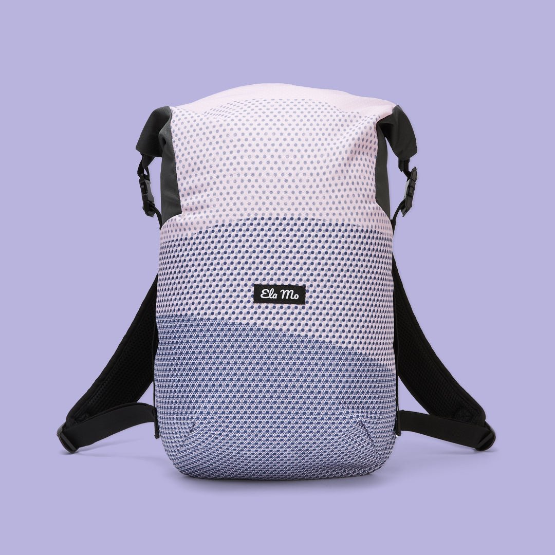 Ela Mo™ Rolltop Lite | New Horizon. Rucksack in Blautönen mit Herstellerlogo auf der Vorderseite, vor helllila Hintergrund.