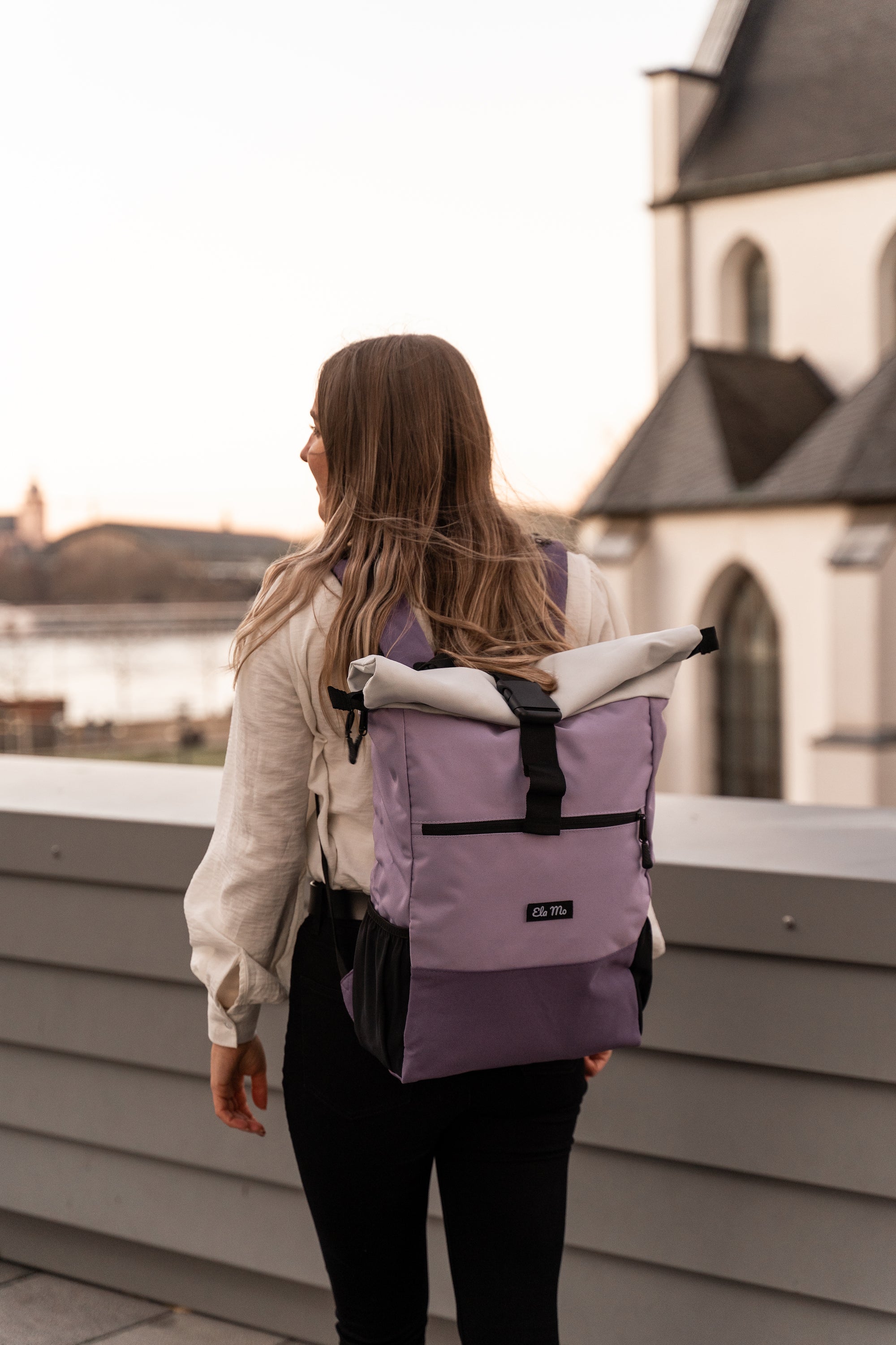 Ela Mo™ Rolltop Rucksack | Lavender. Eine Frau mit dem lila Rucksack auf der Wiese.