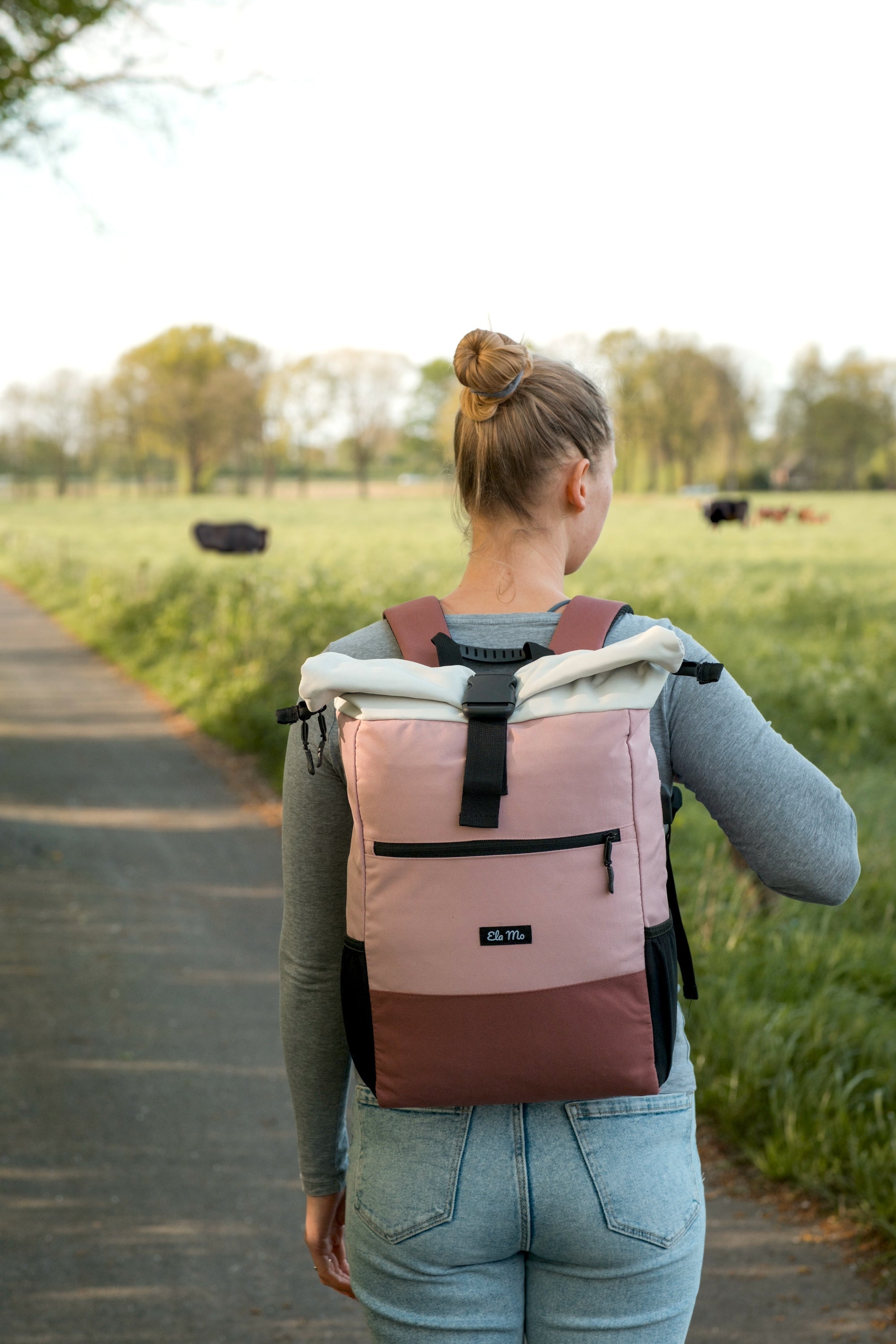 Ela Mo™ Rolltop Rucksack | Strawberry Cream. Eine Frau mit dem rosa Rucksack auf der Wiese.