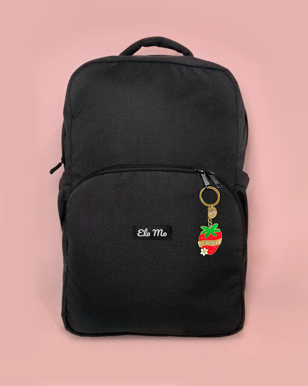 Ela Mo™ Schlüsselanhänger | Erdbeere. Schlüsselanhänger in Form einer Erdbeere am Reißverschluss des schwarzen Rucksacks.