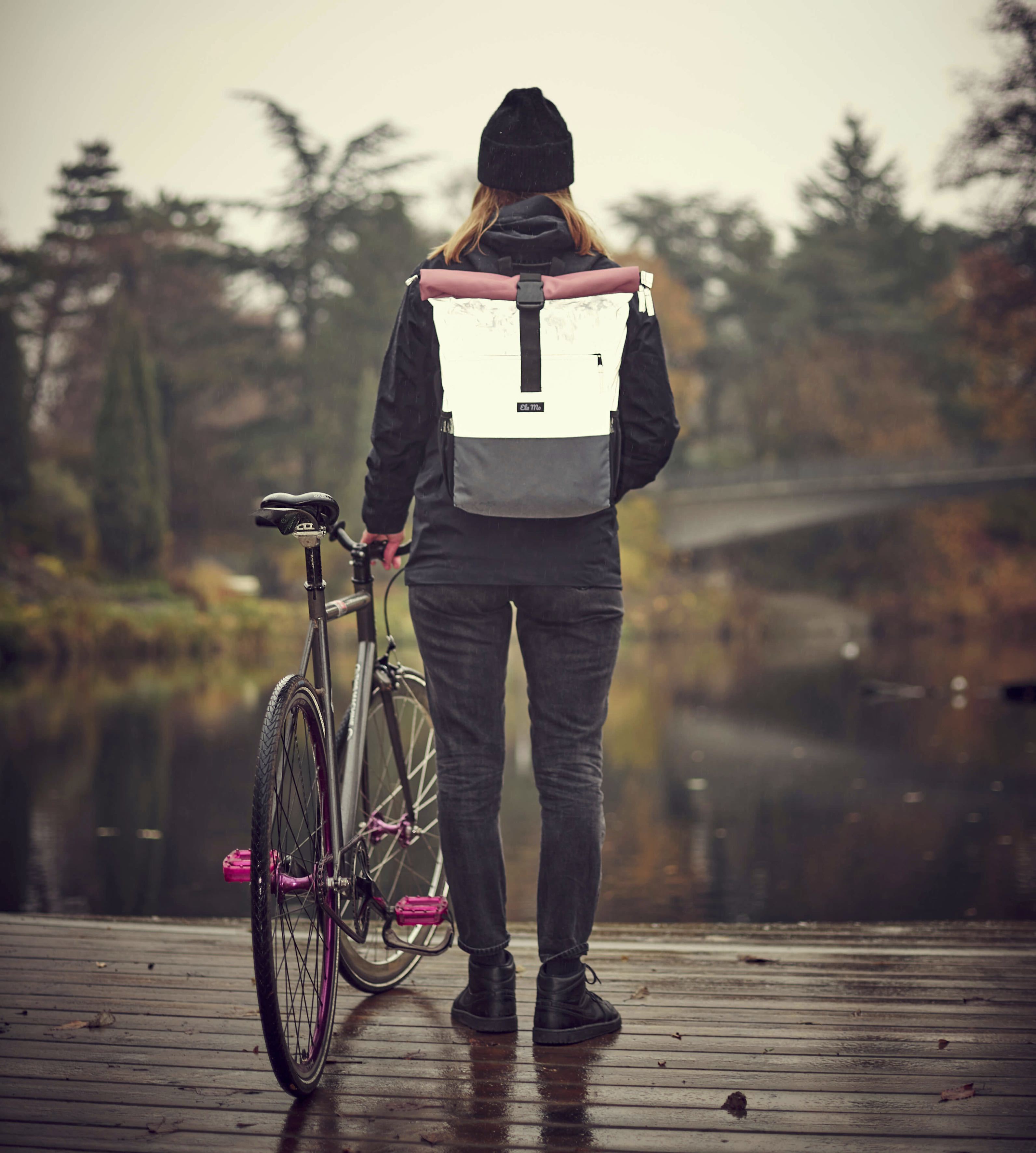 Ela Mo™ Rolltop Rucksack Night Edition | Peach. Eine Frau mit dem reflektiven Rucksack auf dem Rücken im Freien.