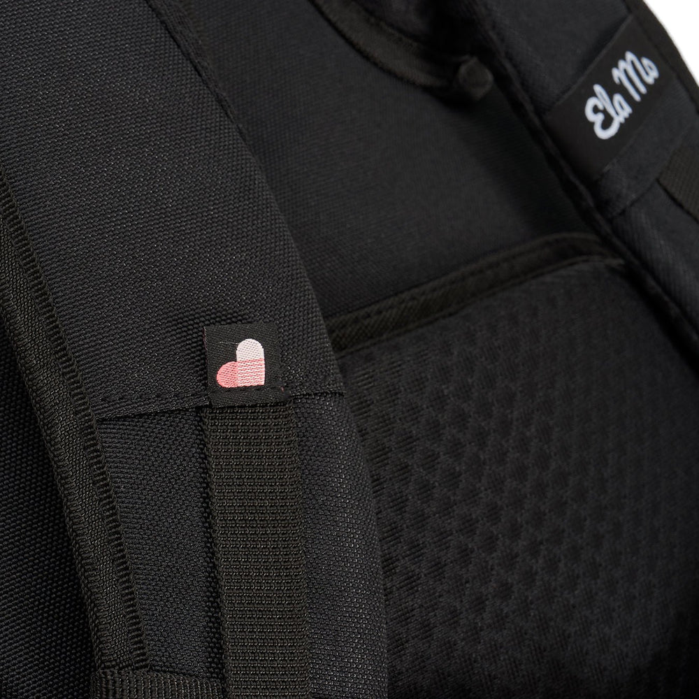 Ela Mo™ Everywhere Daypack | Black. Schulterriemen des schwarzen Rucksacks mit kleinen Herzchen und Herstellerlogo darauf.