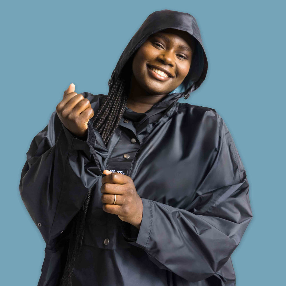 Ela Mo™ Regenponcho | Black. Eine Frau mit Regenponcho und Kapuze auf dem Kopf.