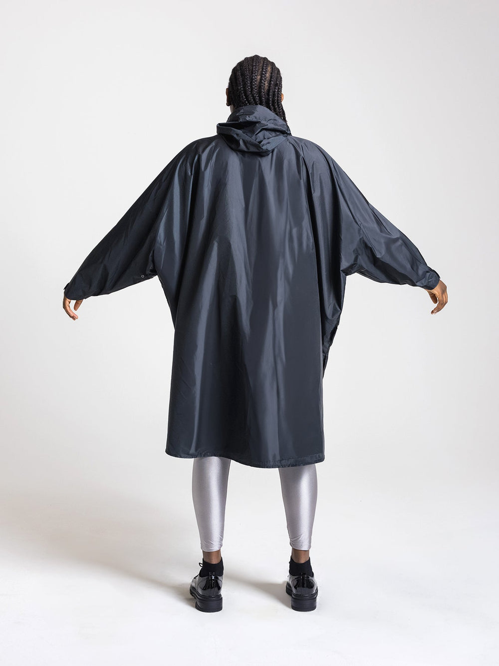 Ela Mo™ Regenponcho | Black. Frau mit Regenponcho von hinten auf weißem Hintergrund.