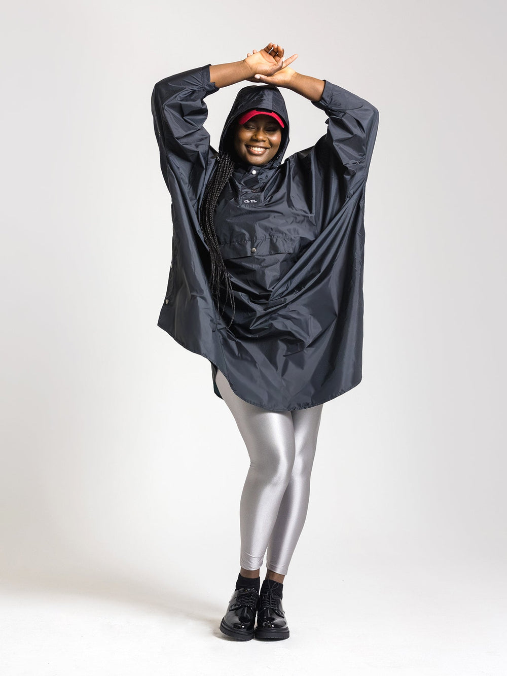 Ela Mo™ Regenponcho | Black. Lachende Frau mit Regenponcho und Kapuze.