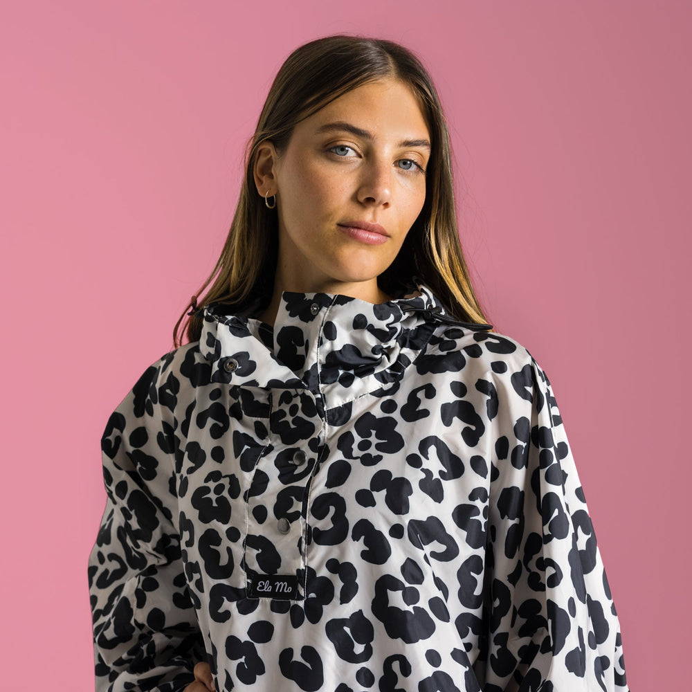 Ela Mo™ Regenponcho | Leo. Eine Frau mit Regenponcho auf rosa Hintergund.