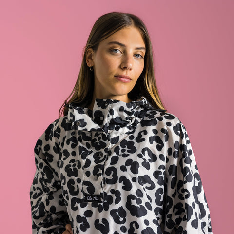 Ela Mo™ Regenponcho | Leo. Eine Frau mit Regenponcho auf rosa Hintergund.