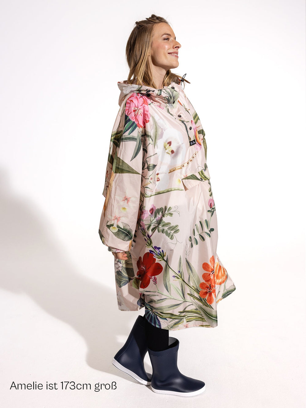 Ela Mo™ Regenponcho | Luxe. Eine Frau im Regenponcho, mit Angabe ihrer Körpergröße.