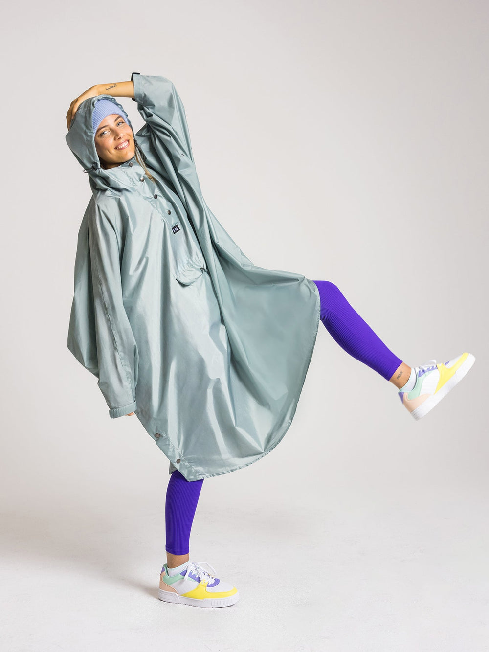 Ela Mo™ Regenponcho | Mint. Lachende Frau mit Regenponcho und Kapuze.
