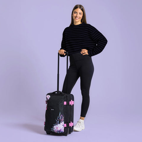 Ela Mo™ Reisetasche mit Rollen 42 Liter | Beauty in Darkness. Eine Frau neben einer Reisetasche mit hochgezogenem Griff.
