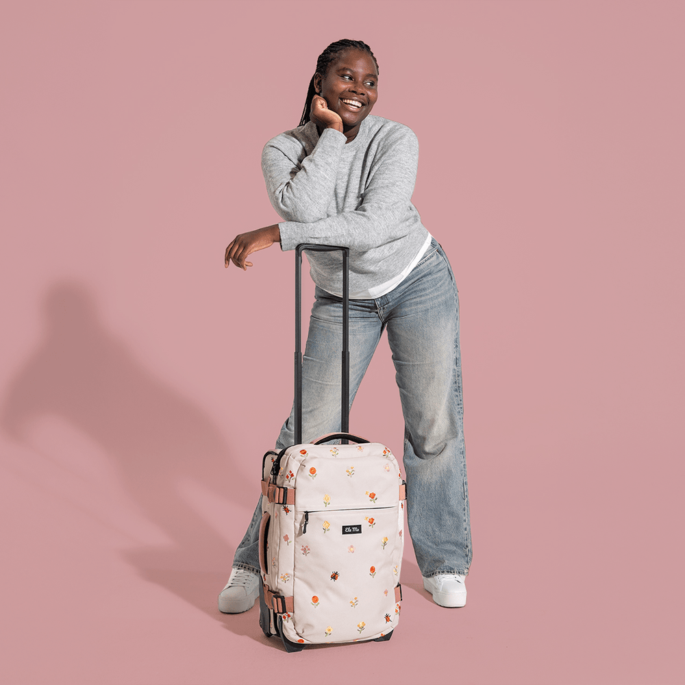 Ela Mo™ Reisetasche mit Rollen 42 Liter | Embroidery Edition Losy. Frau mit der geblümten Tasche und hochgezogenem Griff.