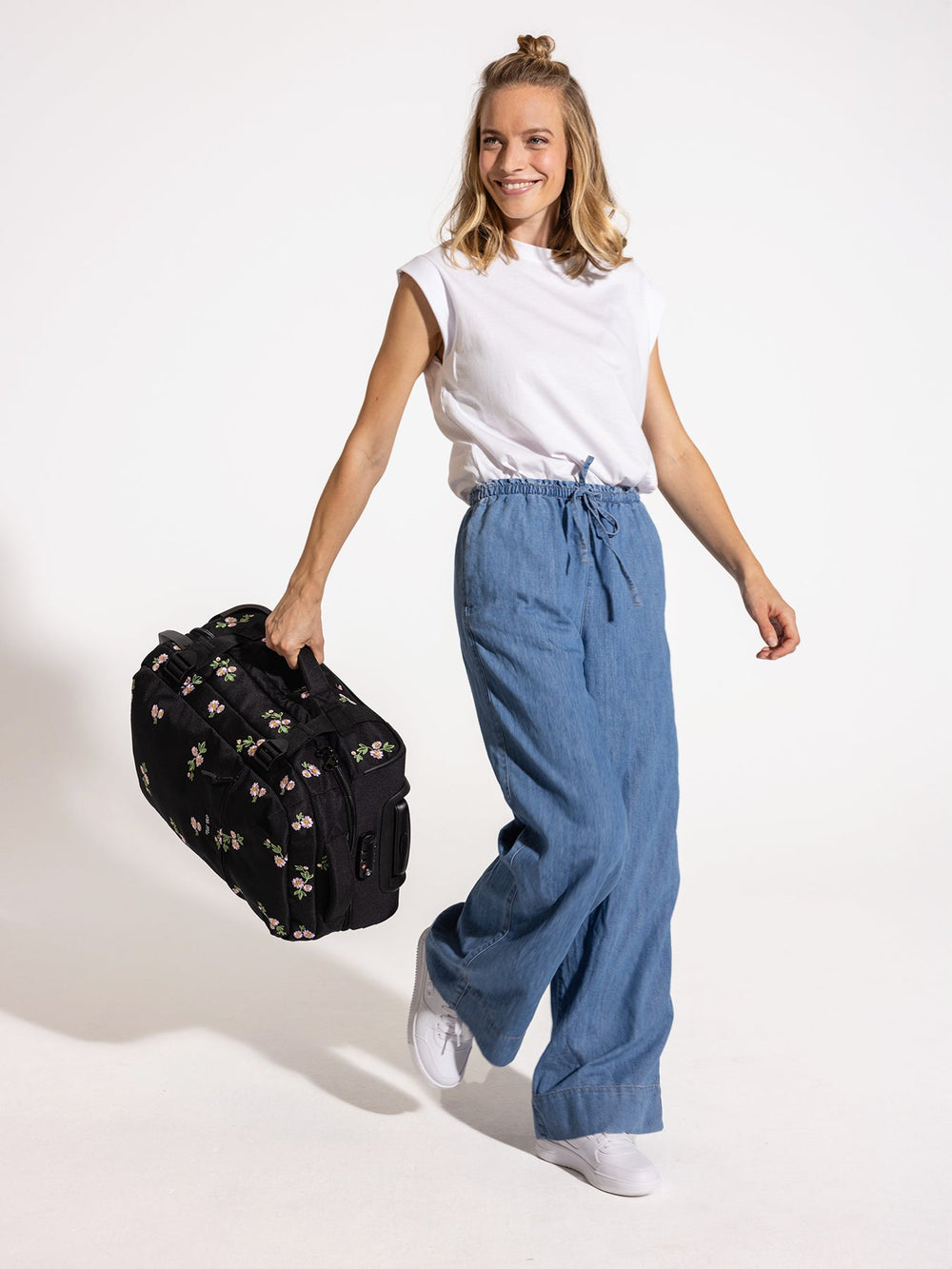 Ela Mo™ Reisetasche mit Rollen 42 Liter | Embroidery Edition Upsy Daisy. Frau mit floral gemusterter Tasche am Seitengriff.