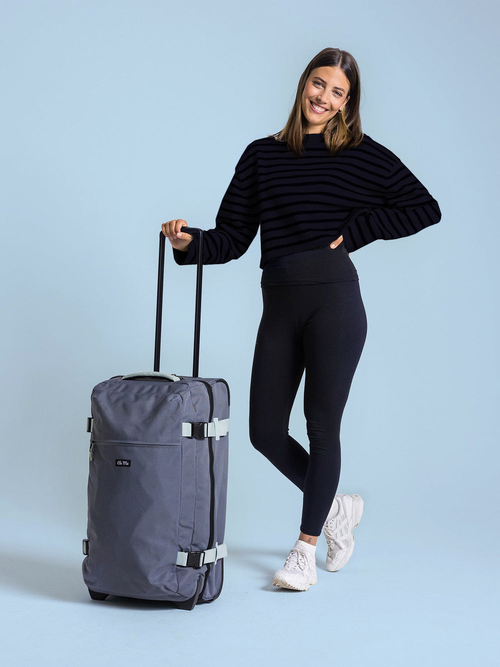 Ela Mo™ Reisetasche mit Rollen 78 Liter | Darkgrey Mint. Eine Frau neben einer Reisetasche mit hochgezogenem Griff.
